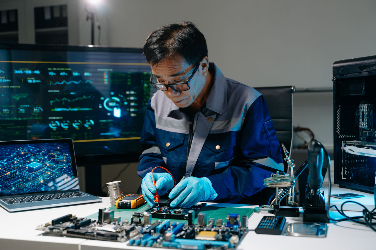 Professional technician repairing hard drive with multimeter at high-tech electronics workstation with data monitors